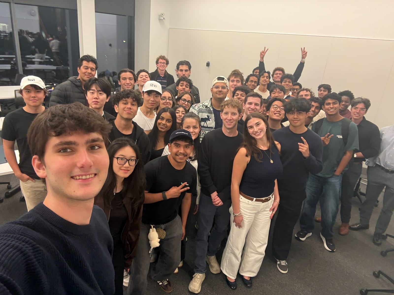 A group selfie of about forty students packed into a classroom, smiling and throwing peace signs at the camera.