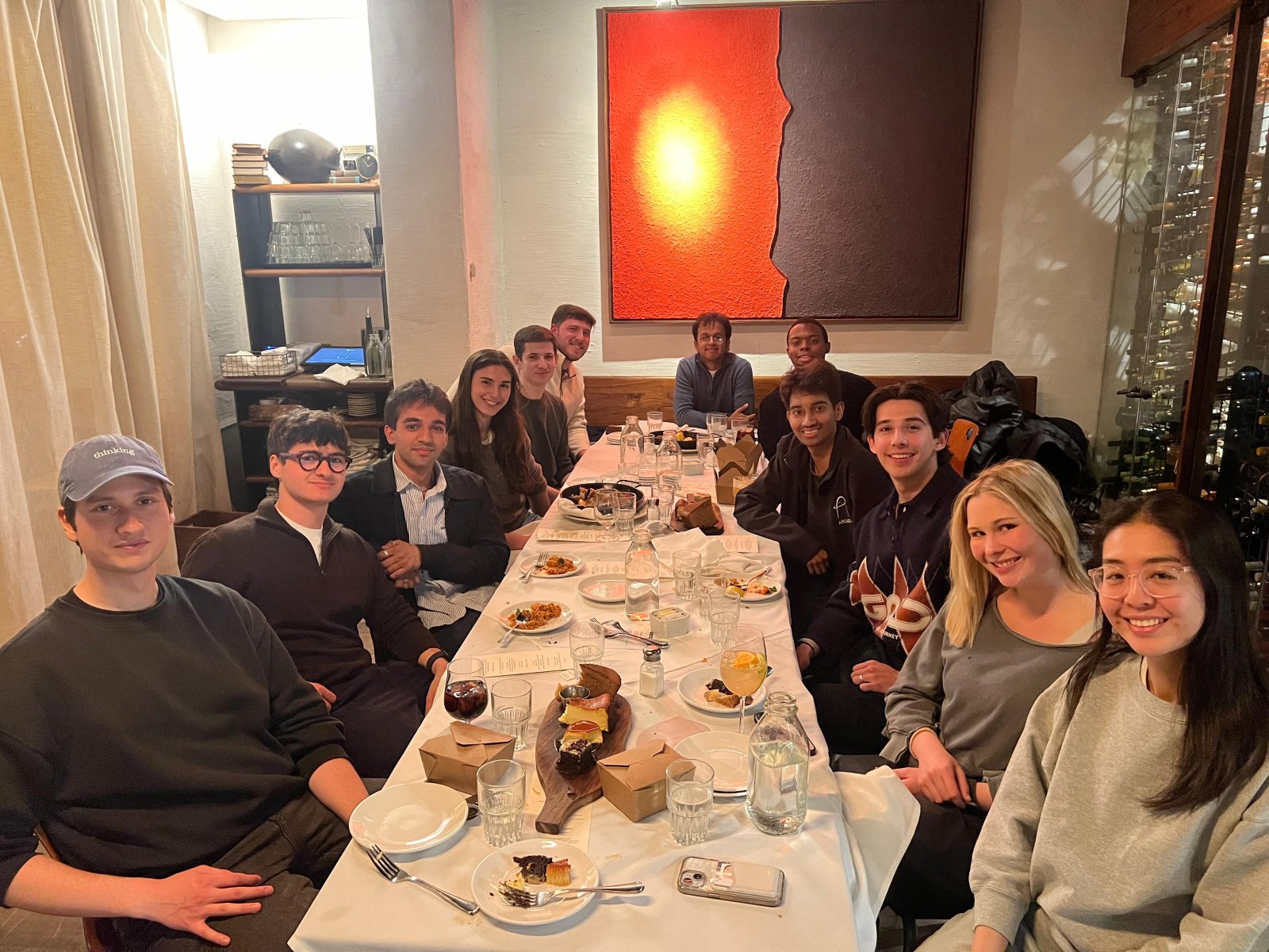 A long table of people turning to face the camera at a restaurant dinner.