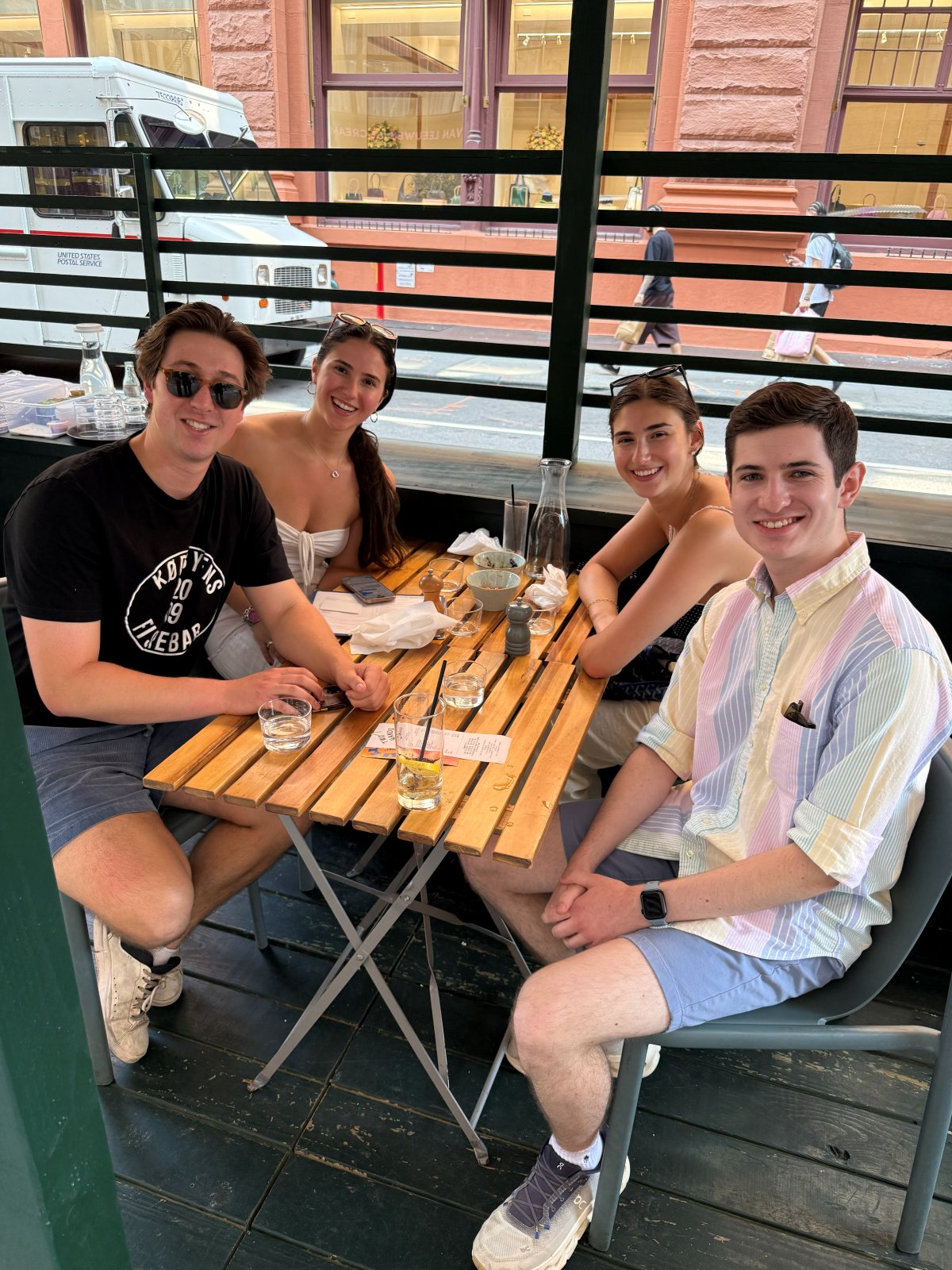 Four people around a small wooden table on a restaurant patio in SoHo.