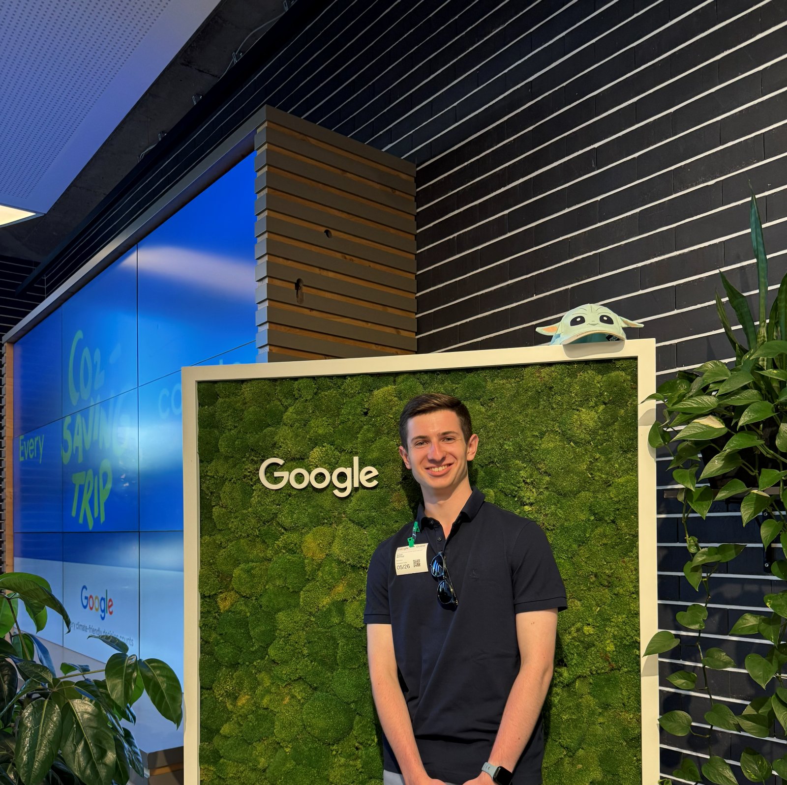 Noah in front of a moss wall with the Google logo, beside a screen reading Every CO2 saving trip counts.
